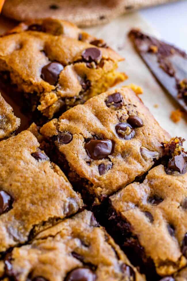 pumpkin bars with chocolate chips on parchment paper with a knife in the background.