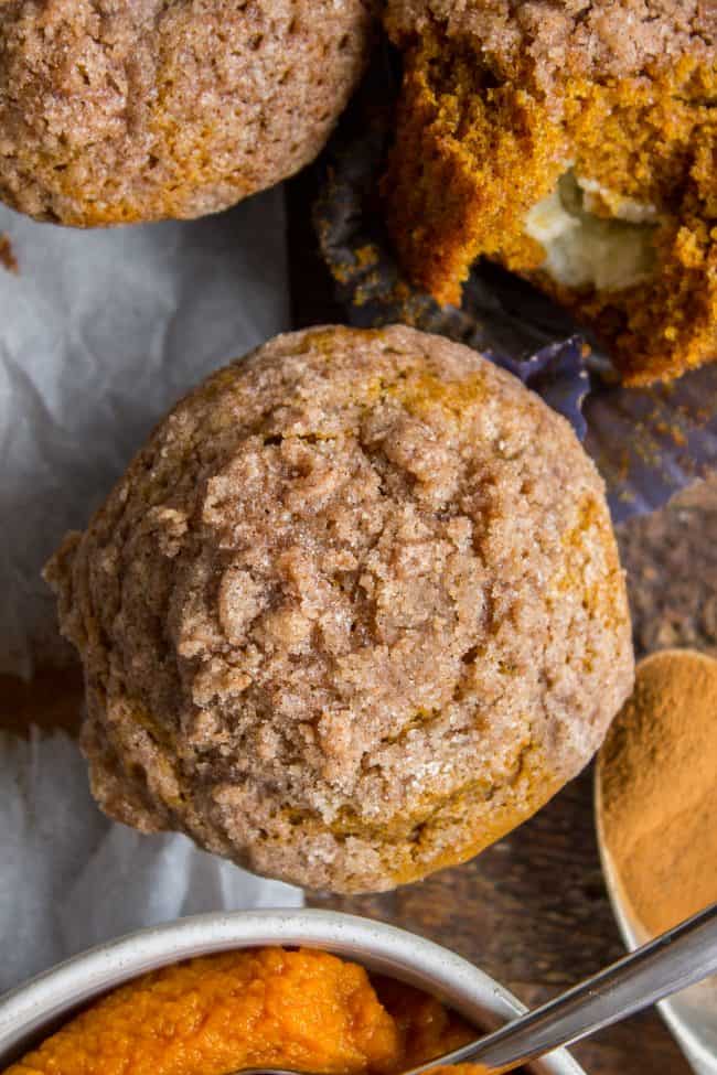 Pumpkin Cream Cheese Muffins from The Food Charlatan. There is no better way to welcome fall than with these Pumpkin Cream Cheese Muffins! A moist, tender, ultra pumpkin-y muffin, filled with sweetened cream cheese, and topped with cinnamon sugar crunch topping! They are irresistible! If it's too hot where you are, these muffins are guaranteed to make the leaves start falling off your trees. #muffin #pumpkin #fall #fallbaking #creamcheese #filling #filled #crumbtopping #topping #best #moist #cinnamon #pumpkinpie #pumpkinpiespice #thanksgiving #autumn #starbucks #copycat #tall #baking overhead of pumpkin cream cheese muffins on a counter.