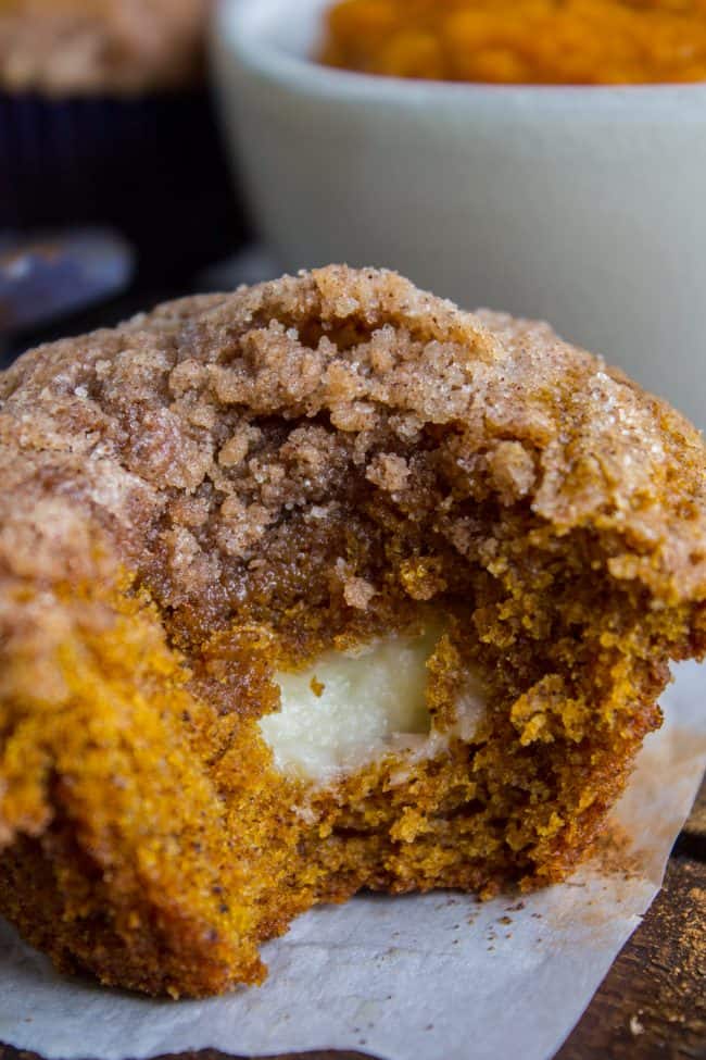 Pumpkin Cream Cheese Muffins from The Food Charlatan. There is no better way to welcome fall than with these Pumpkin Cream Cheese Muffins! A moist, tender, ultra pumpkin-y muffin, filled with sweetened cream cheese, and topped with cinnamon sugar crunch topping! They are irresistible! #muffin #pumpkin #fall #fallbaking #creamcheese #filling #filled #crumbtopping #topping #best #moist #cinnamon #pumpkinpie #pumpkinpiespice #thanksgiving #autumn #starbucks #copycat #tall #baking side view of a cream cheese pumpkin muffins with a bite taken out.