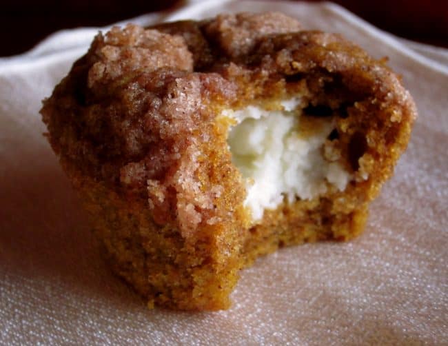 Pumpkin Cream Cheese Muffins from The Food Charlatan. There is no better way to welcome fall than with these Pumpkin Cream Cheese Muffins! A moist, tender, ultra pumpkin-y muffin, filled with sweetened cream cheese, and topped with cinnamon sugar crunch topping! They are irresistible! If it's too hot where you are, these muffins are guaranteed to make the leaves start falling off your trees. #muffin #pumpkin #fall #fallbaking #creamcheese #filling #filled #crumbtopping #topping #best #moist #cinnamon #pumpkinpie #pumpkinpiespice #thanksgiving #autumn #starbucks #copycat #tall #baking recipe for pumpkin cream cheese muffins with a bite taken out.