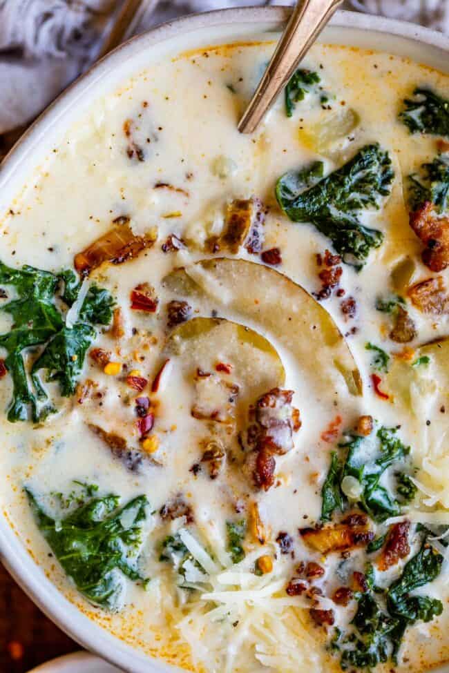 Zuppa Toscana Copycat (Sausage, Potato, and Kale Soup) From The Food Charlatan. Zuppa Toscana is a rich and creamy, soul-satisfying soup made with Italian sausage, potatoes, and hearty kale. It’s a copycat recipe of the famous soup at Olive Garden. I could eat this stuff for days! #zuppatoscana #soup #easy #recipe #olivegarden #onepot #zuppa #toscana #copycat #copy #sausage #potatoes #creamy #cream #halloween #fallsoup #fall #hearty #kale #italiansausage #betterthan Zuppa Toscana recipe in a white bowl with spoon and Italian sausage
