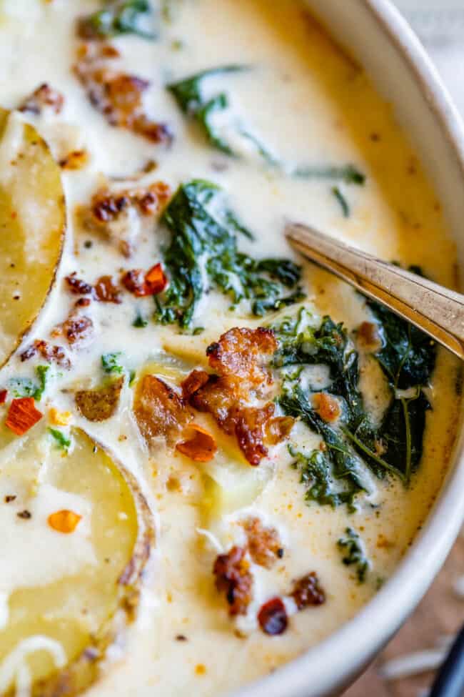 Zuppa Toscana Copycat (Sausage, Potato, and Kale Soup) From The Food Charlatan. Zuppa Toscana is a rich and creamy, soul-satisfying soup made with Italian sausage, potatoes, and hearty kale. It’s a copycat recipe of the famous soup at Olive Garden. I could eat this stuff for days! #zuppatoscana #soup #easy #recipe #olivegarden #onepot #zuppa #toscana #copycat #copy #sausage #potatoes #creamy #cream #halloween #fallsoup #fall #hearty #kale #italiansausage #betterthan Olive Garden Zuppa Toscana in a white bowl with sausage and kale