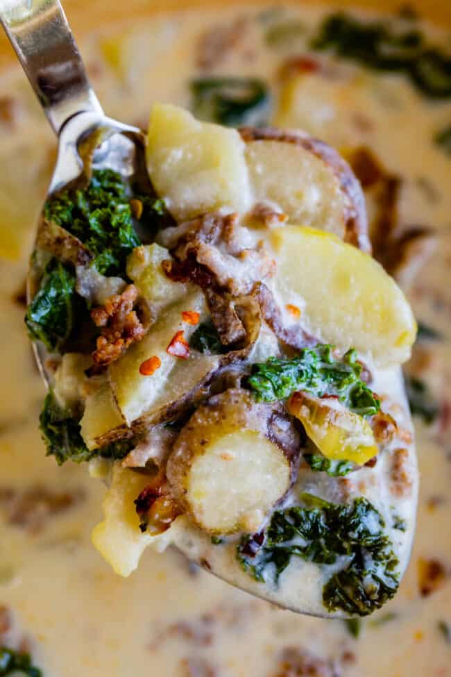 Zuppa Toscana Copycat (Sausage, Potato, and Kale Soup) From The Food Charlatan. Zuppa Toscana is a rich and creamy, soul-satisfying soup made with Italian sausage, potatoes, and hearty kale. It’s a copycat recipe of the famous soup at Olive Garden. I could eat this stuff for days! #zuppatoscana #soup #easy #recipe #olivegarden #onepot #zuppa #toscana #copycat #copy #sausage #potatoes #creamy #cream #halloween #fallsoup #fall #hearty #kale #italiansausage #betterthan zuppa toscana soup recipe held up on a serving spoon with potatoes kale and sausage