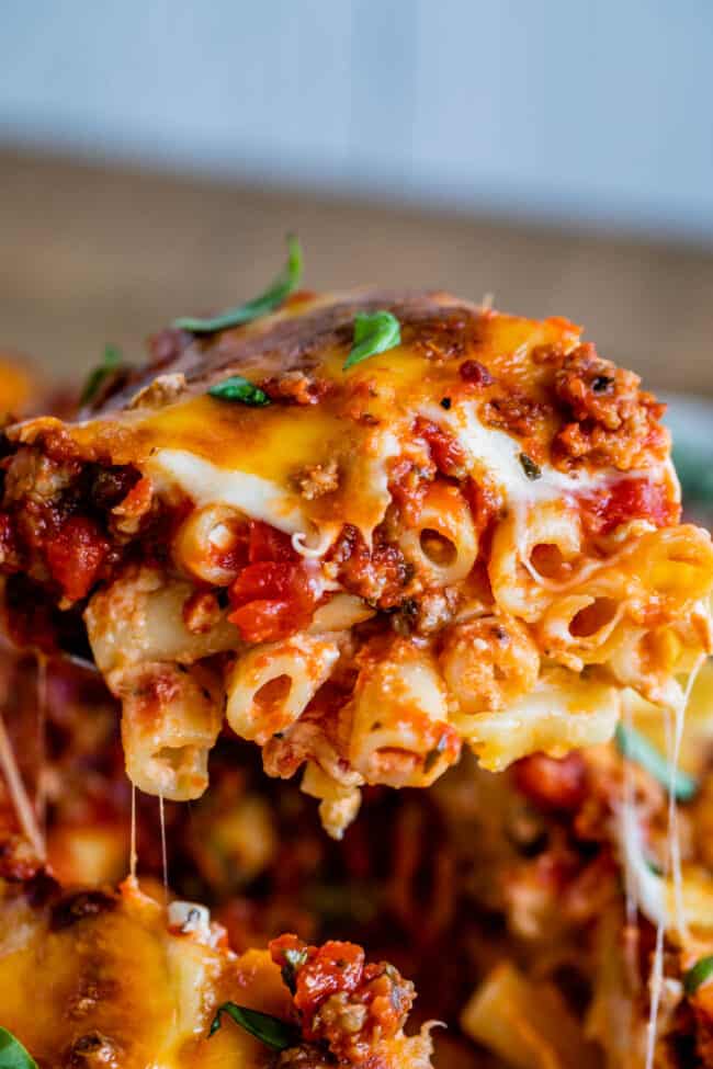 The Best Baked Ziti from The Food Charlatan. This recipe is a favorite! Italian sausage marinara, cottage cheese, and fresh basil combine to make this decadent casserole. The best part is the mozzarella that's chopped instead of shredded. They melt into pools of cheesy glory. We've always called it "Postpartum Ziti" because it makes a TON and is perfect for bringing to new moms! #bakedziti #pasta #ziti #easy #recipe #marinara #italiansausage #best #foracrowd #classic #cheesy #mozzarella a piece of baked ziti with stretchy melted cheese.