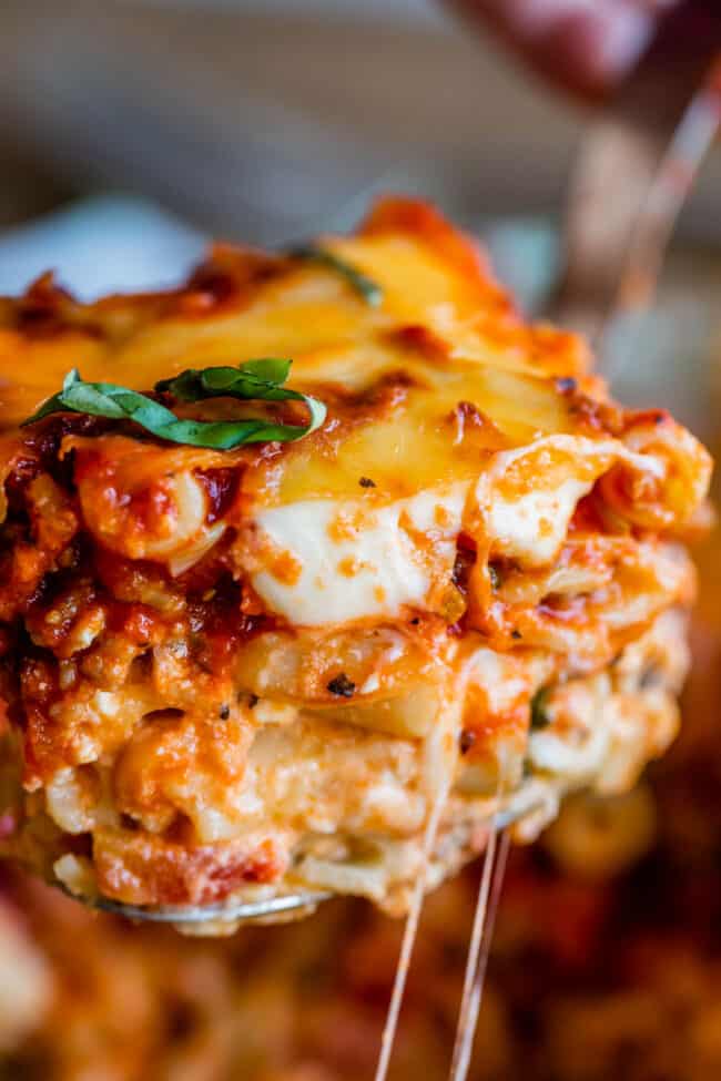 The Best Baked Ziti from The Food Charlatan. This recipe is a favorite! Italian sausage marinara, cottage cheese, and fresh basil combine to make this decadent casserole. The best part is the mozzarella that's chopped instead of shredded. They melt into pools of cheesy glory. We've always called it "Postpartum Ziti" because it makes a TON and is perfect for bringing to new moms! #bakedziti #pasta #ziti #easy #recipe #marinara #italiansausage #best #foracrowd #classic #cheesy #mozzarella a slice of baked ziti lifted by a serving spoon.