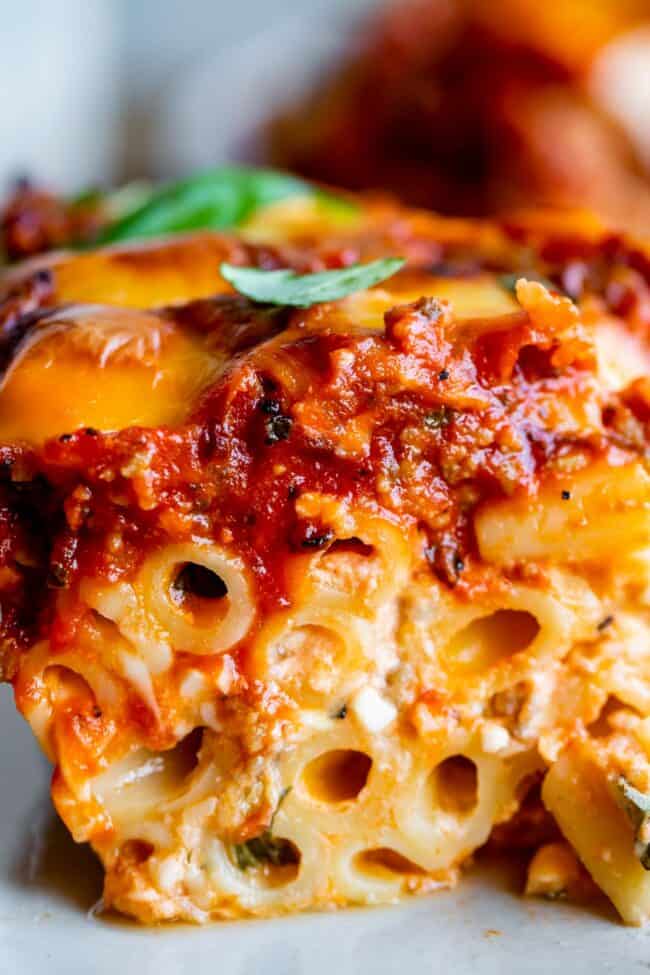 The Best Baked Ziti from The Food Charlatan. This recipe is a favorite! Italian sausage marinara, cottage cheese, and fresh basil combine to make this decadent casserole. The best part is the mozzarella that's chopped instead of shredded. They melt into pools of cheesy glory. We've always called it "Postpartum Ziti" because it makes a TON and is perfect for bringing to new moms! #bakedziti #pasta #ziti #easy #recipe #marinara #italiansausage #best #foracrowd #classic #cheesy #mozzarella baked ziti shot from the side.