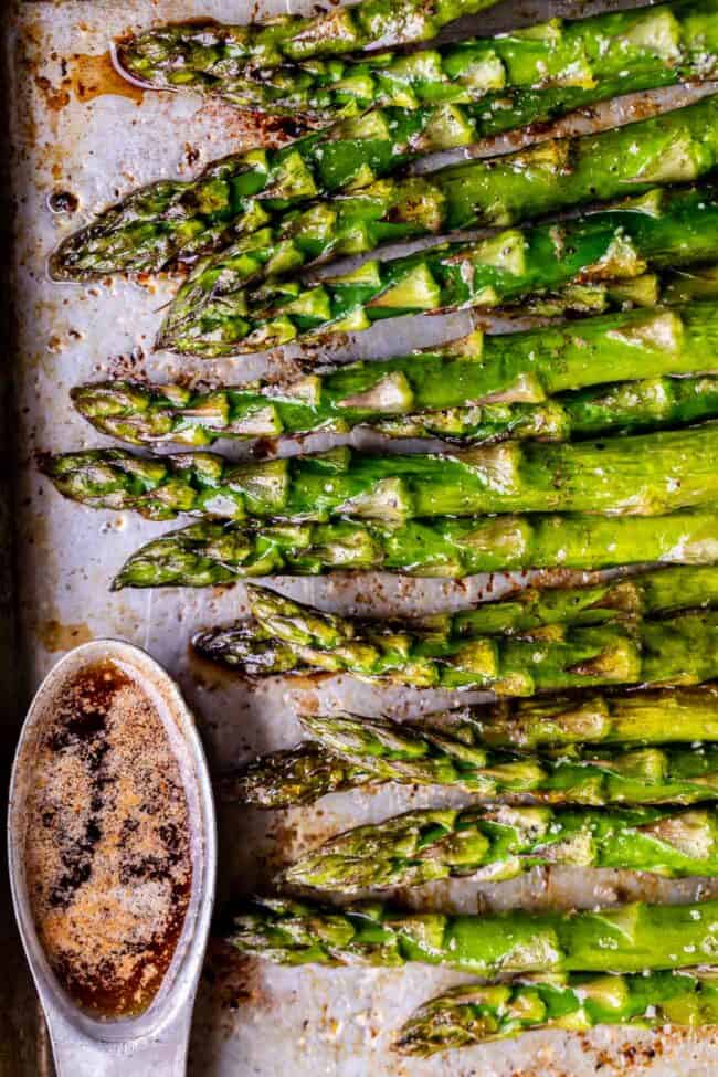 roasted asparagus on a baking sheet with a ramekin of browned butter. 