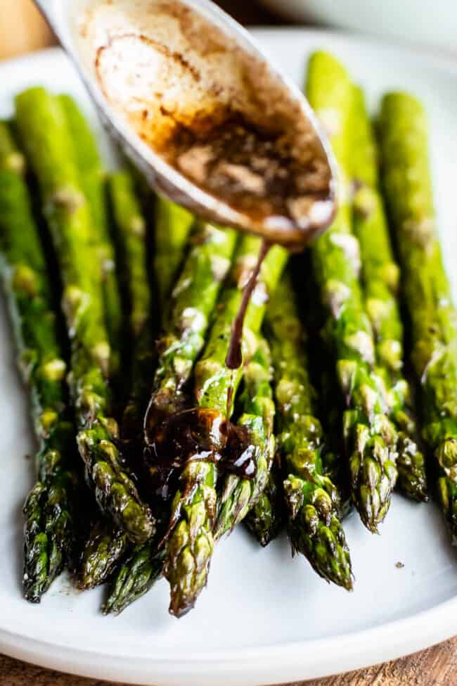 oven roasted asparagus on a white plate with a spoonful of browned balsamic butter. 