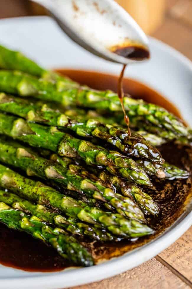 roasted asparagus with browned balsamic butter being drizzled from a spoon. 