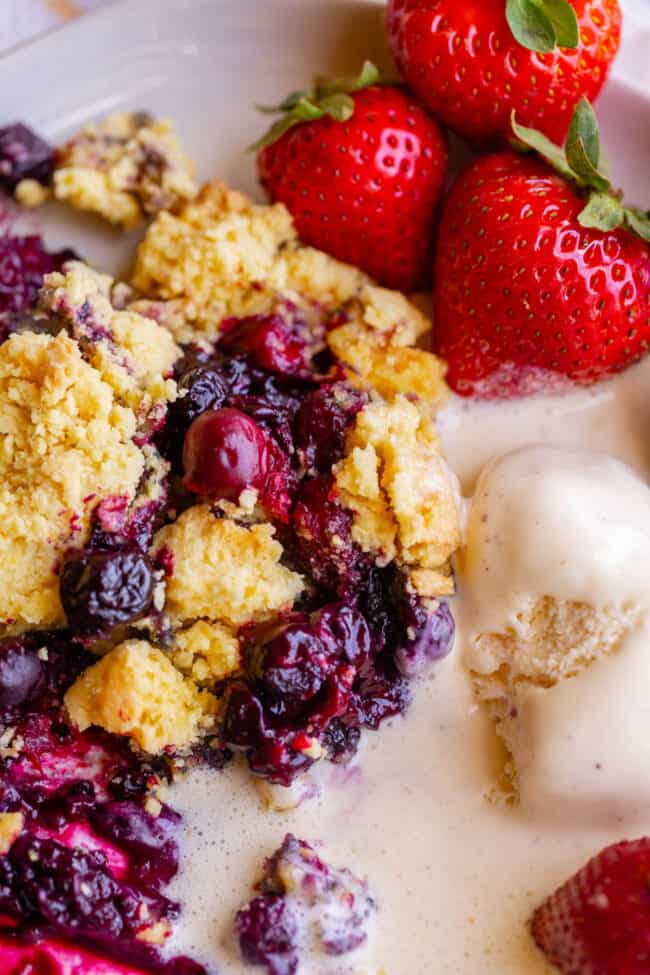 berry cobbler on a plate with strawberries and ice cream.
