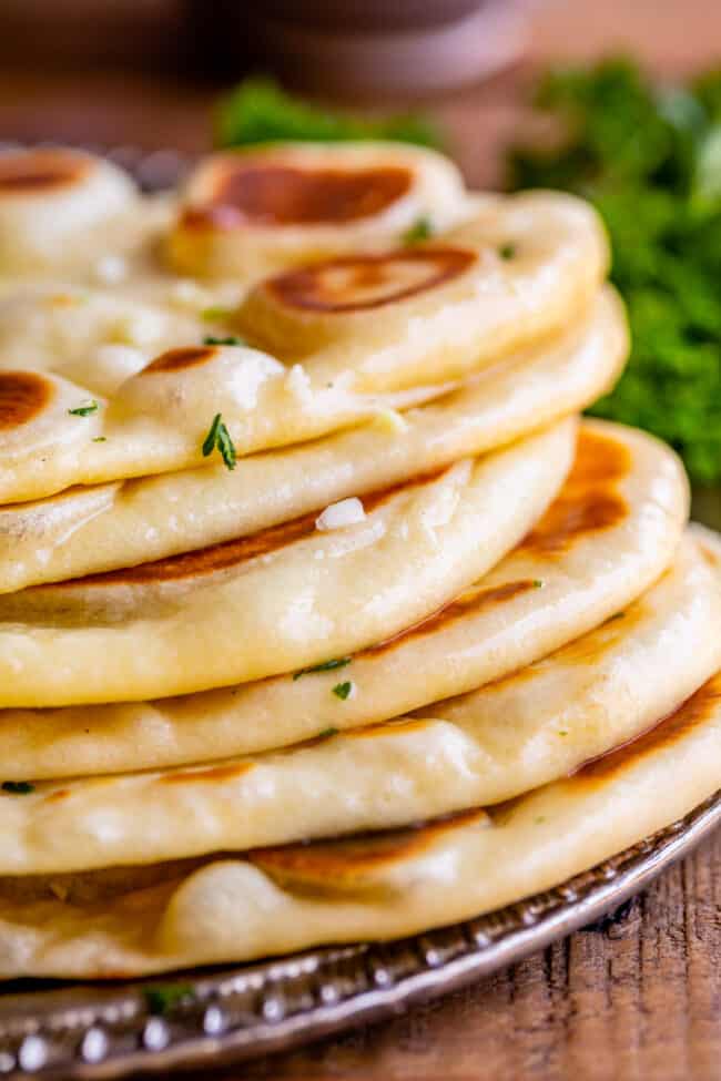 Homemade Naan Bread Recipe from The Food Charlatan. Make restaurant quality Naan Bread at home! If you have never tasted a fresh, tender, buttery homemade naan, you're totally missing out. I will show you just how easy this recipe is to put together and gives you the perfect receptacle for cleaning up all the curry on your plate! #naan #Indian #easy #recipe #curry #breadrecipe #yeast #garlic #homemade #flatbread #yogurt #parsley #sidedish #bread fresh homemade buttery naan, stacked on a plate.
