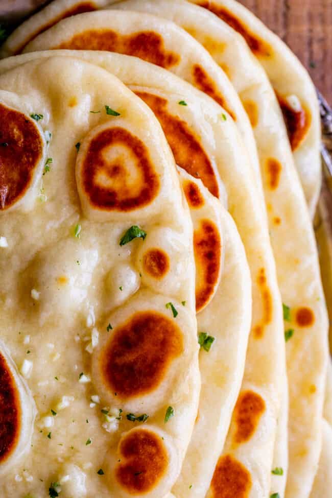 Homemade Naan Bread Recipe from The Food Charlatan. Make restaurant quality Naan Bread at home! If you have never tasted a fresh, tender, buttery homemade naan, you're totally missing out. I will show you just how easy this recipe is to put together and gives you the perfect receptacle for cleaning up all the curry on your plate! #naan #Indian #easy #recipe #curry #breadrecipe #yeast #garlic #homemade #flatbread #yogurt #parsley #sidedish #bread buttered homemade naan with garlic and fresh parsley stacked up, shot from above.