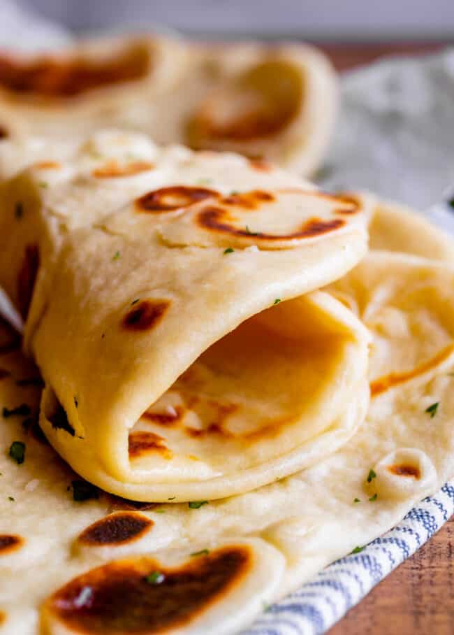 Homemade Naan Bread Recipe from The Food Charlatan. Make restaurant quality Naan Bread at home! If you have never tasted a fresh, tender, buttery homemade naan, you're totally missing out. I will show you just how easy this recipe is to put together and gives you the perfect receptacle for cleaning up all the curry on your plate! #naan #Indian #easy #recipe #curry #breadrecipe #yeast #garlic #homemade #flatbread #yogurt #parsley #sidedish #bread homemade naan bread rolled up on a blue and white striped towel.