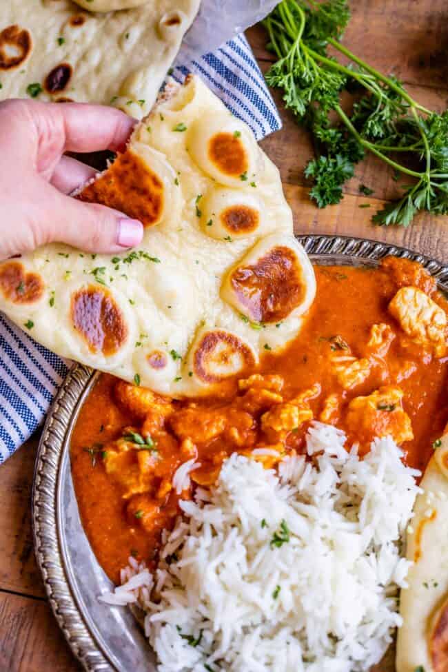 Homemade Naan Bread Recipe from The Food Charlatan. Make restaurant quality Naan Bread at home! If you have never tasted a fresh, tender, buttery homemade naan, you're totally missing out. I will show you just how easy this recipe is to put together and gives you the perfect receptacle for cleaning up all the curry on your plate! #naan #Indian #easy #recipe #curry #breadrecipe #yeast #garlic #homemade #flatbread #yogurt #parsley #sidedish #bread a hand dipping homemade naan into chicken curry next to white rice on a plate.