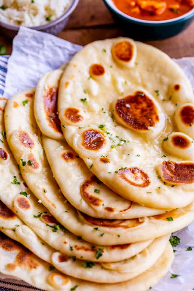 Homemade Naan Bread Recipe from The Food Charlatan. Make restaurant quality Naan Bread at home! If you have never tasted a fresh, tender, buttery homemade naan, you're totally missing out. I will show you just how easy this recipe is to put together and gives you the perfect receptacle for cleaning up all the curry on your plate! #naan #Indian #easy #recipe #curry #breadrecipe #yeast #garlic #homemade #flatbread #yogurt #parsley #sidedish #bread several buttered naan breads on a piece of parchment paper, sprinkled with fresh parsley.