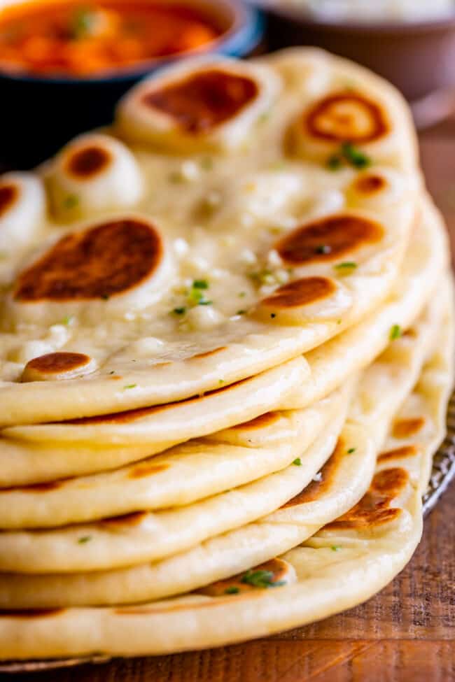Homemade Naan Bread Recipe from The Food Charlatan. Make restaurant quality Naan Bread at home! If you have never tasted a fresh, tender, buttery homemade naan, you're totally missing out. I will show you just how easy this recipe is to put together and gives you the perfect receptacle for cleaning up all the curry on your plate! #naan #Indian #easy #recipe #curry #breadrecipe #yeast #garlic #homemade #flatbread #yogurt #parsley #sidedish #bread freshly buttered naan bread stacked on a plate.