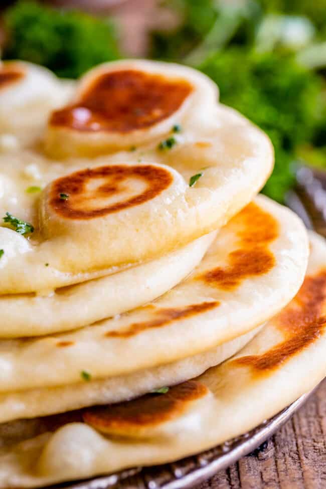 Homemade Naan Bread Recipe from The Food Charlatan. Make restaurant quality Naan Bread at home! If you have never tasted a fresh, tender, buttery homemade naan, you're totally missing out. I will show you just how easy this recipe is to put together and gives you the perfect receptacle for cleaning up all the curry on your plate! #naan #Indian #easy #recipe #curry #breadrecipe #yeast #garlic #homemade #flatbread #yogurt #parsley #sidedish #bread fresh homemade naan bread, stacked up on a plate.