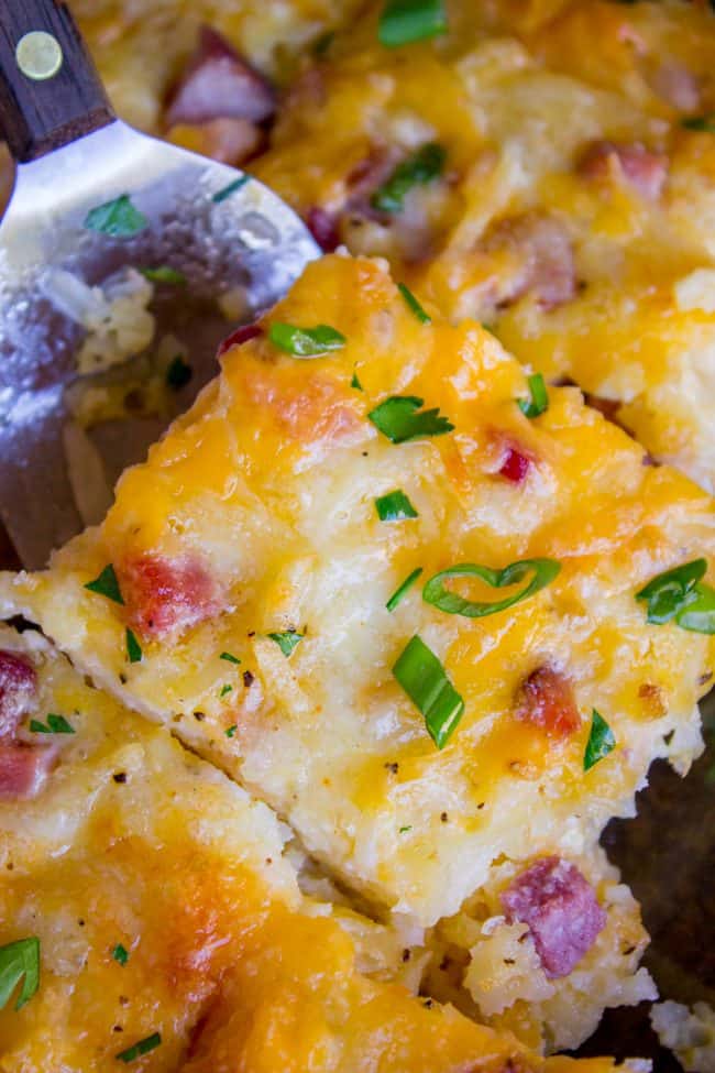 Cheesy Overnight Hashbrown Breakfast Casserole from The Food Charlatan. This Cheesy Hashbrown Breakfast Casserole is everything you need on Christmas morning! Hashbrowns are baked til crispy, then topped with eggs, cheese, and black forest ham. It's an overnight recipe to boot! Make ahead breakfasts ftw. #makeahead #cheese #breakfast #casserole #breakfastcasserole #easy #recipe #ham #blackforestham #Christmas #party #holildays #withhashbrowns #withpotatoes #overnight #makeahead #foracrowd #best hash brown breakfast casserole close-up with chives, ham, cheese, and potatoes visible.