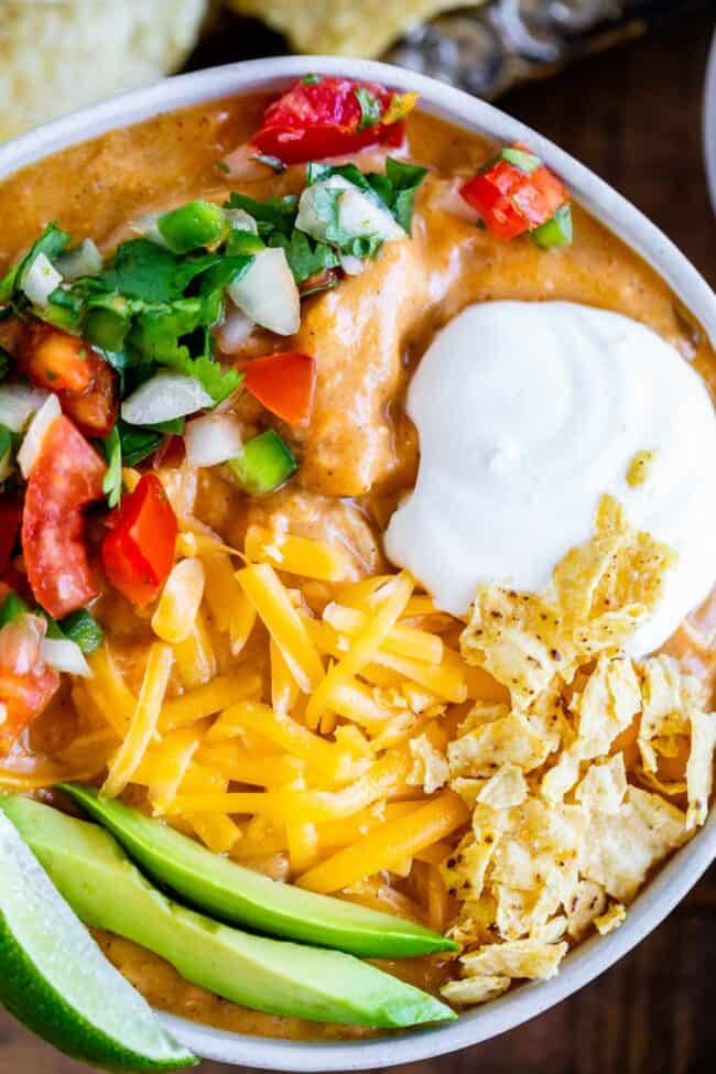 chicken enchilada soup garnished with cheese, chips, avocado, sour cream, and pico de gallo.