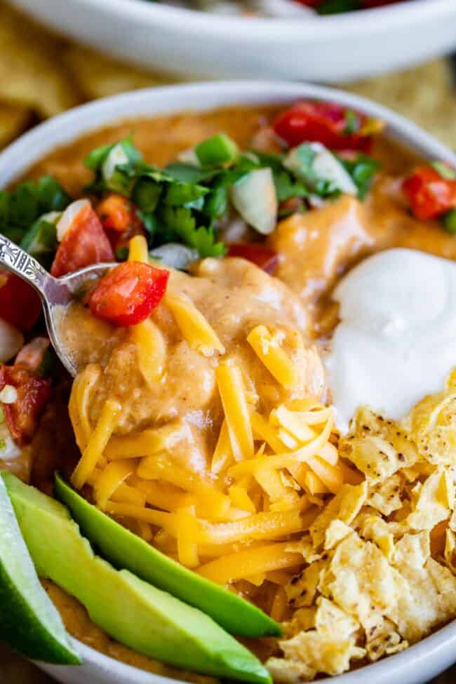 chicken enchilada soup garnished with cheese, chips, avocado, sour cream, and pico de gallo.