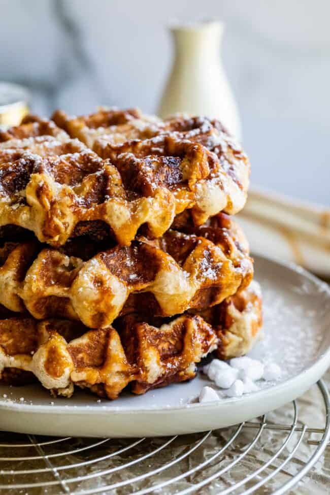 Liege Waffles with Pearl Sugar from The Food Charlatan. Liege waffles are made with a brioche-like yeast dough and are studded with pearl sugar. Pearl sugar is basically a small chunk of sugar that holds its shape as the waffles cooks, leaving you with gloriously crunchy bites of sugar. You can buy these on the street in Belgium and Norway. They make regular waffles look like amateurs. #liege #waffle #pearlsugar #belgium #syrup #maple #easy #recipe #breakfast #brunch #yeast #sugarwaffle a stack of liege waffles with powdered sugar and pearl sugar.