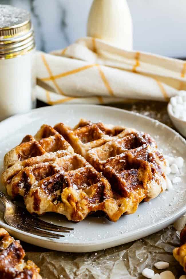 Liege Waffles with Pearl Sugar from The Food Charlatan. Liege waffles are made with a brioche-like yeast dough and are studded with pearl sugar. Pearl sugar is basically a small chunk of sugar that holds its shape as the waffles cooks, leaving you with gloriously crunchy bites of sugar. You can buy these on the street in Belgium and Norway. They make regular waffles look like amateurs. #liege #waffle #pearlsugar #belgium #syrup #maple #easy #recipe #breakfast #brunch #yeast #sugarwaffle liege waffle on a plate with pearl sugar and powdered sugar.