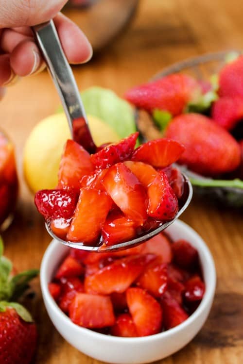 Fresh Strawberry Topping on a spoon with a dish of sauce on a cutting board.