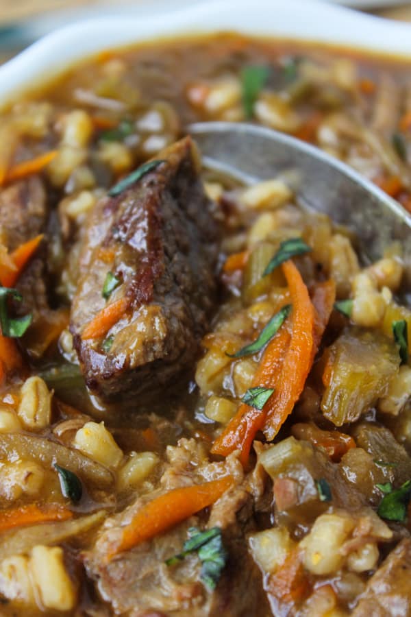 Beef Barley Soup (Slow Cooker) from The Food Charlatan. This soup is lovingly simmered on the stove or in the crock pot to produce the richest Beef Barley Soup recipe I've ever tasted. Shredded carrots and potatoes give it a fabulous, thick texture. #beef #soup #barley #crockpot #slowcooker #vegetable #healthy closeup of crock pot beef barley soup recipe in a large pot.