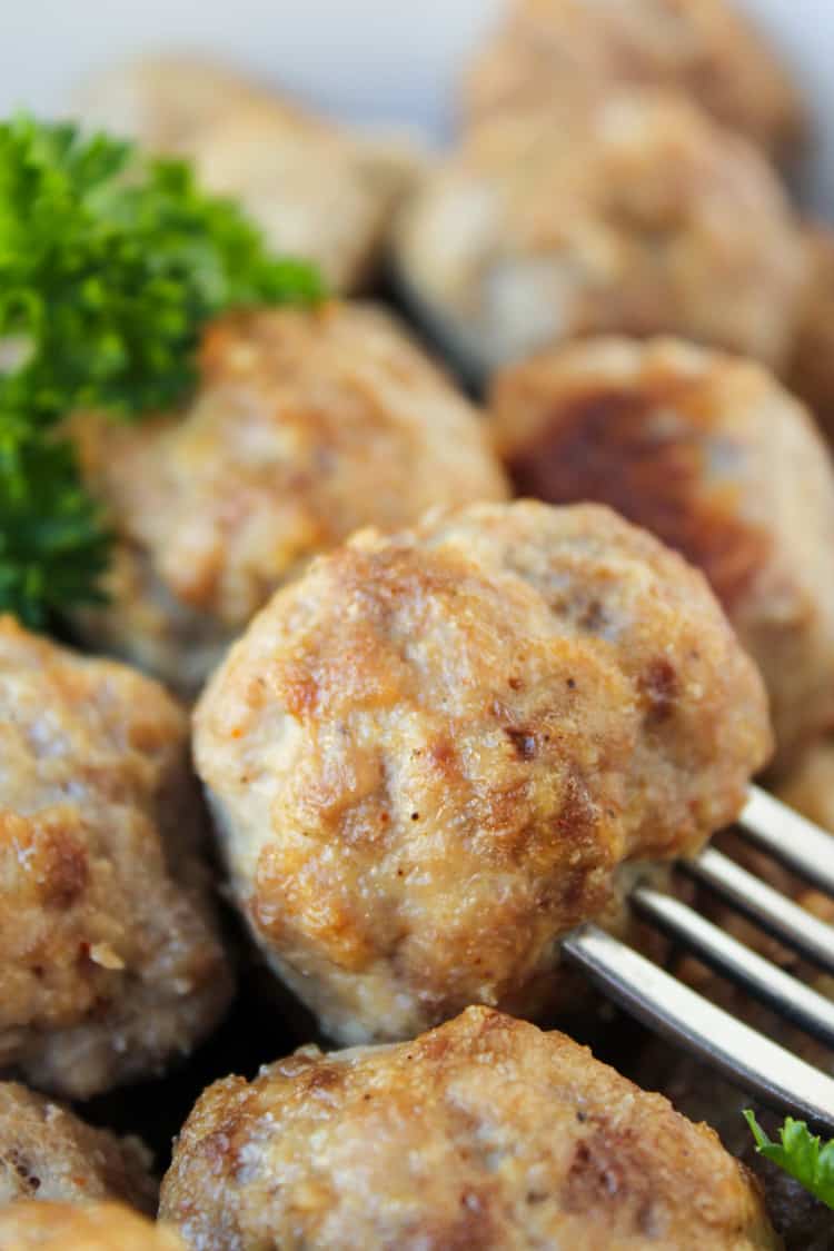 Easy Baked Meatballs from The Food Charlatan. These easy baked meatballs are perfect for making ahead and freezing! They are no-chop, homemade, and very easy to adapt. Skip the overpriced frozen ones at the store! #meatballs #baked #easy #homemade #beef #simple #forspaghetti a fork spearing a baked meatball with parsley garnish.