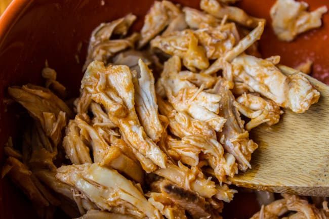 mixing red hot sauce with shredded chicken.