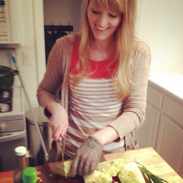 a young woman chopping cabbage with a chef's knife, wearing a chain mail glove. 