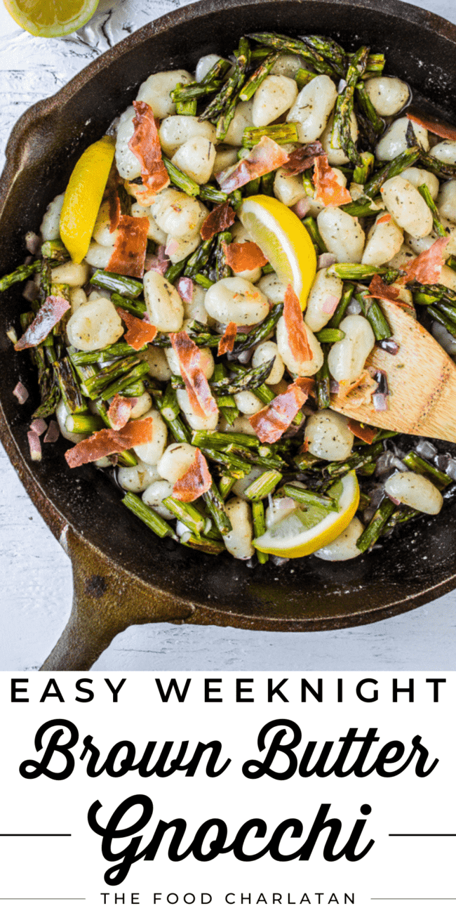 a cast iron skillet with gnocchi, asparagus, lemon slices, and a wooden spoon.