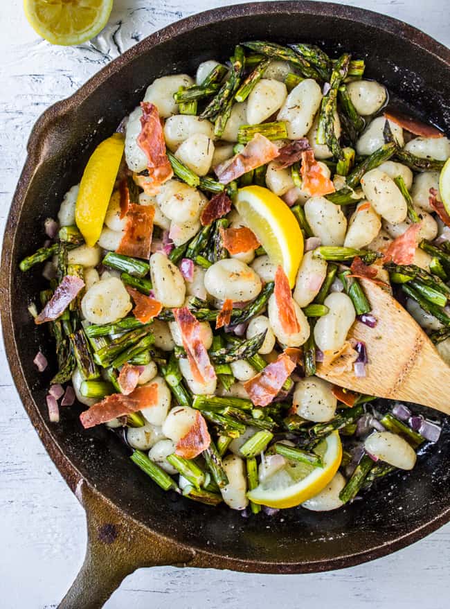 a cast iron pan with gnocchi, lemon slices, asparagus, and prosciutto.