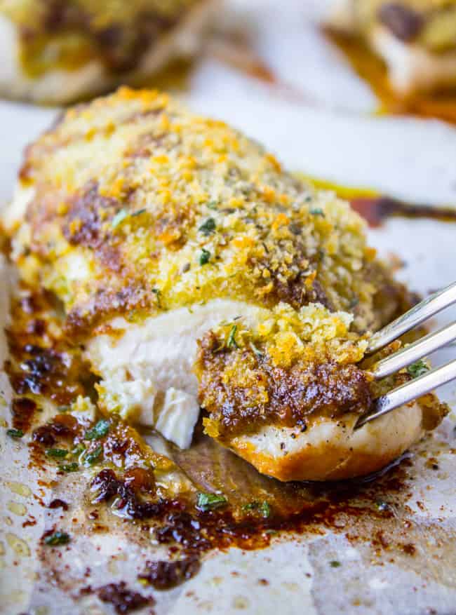 Easy Baked Pesto Chicken from The Food Charlatan. This quick Easy Baked Pesto Chicken recipe comes together in about 30 minutes! Can't beat that. I love it because I almost always have these ingredients on hand so it's a good last minute dinner. #pesto #chicken #baked #basil #oven #healthy #chickenbreast #easy a fork taking a bite of baked pesto chicken.