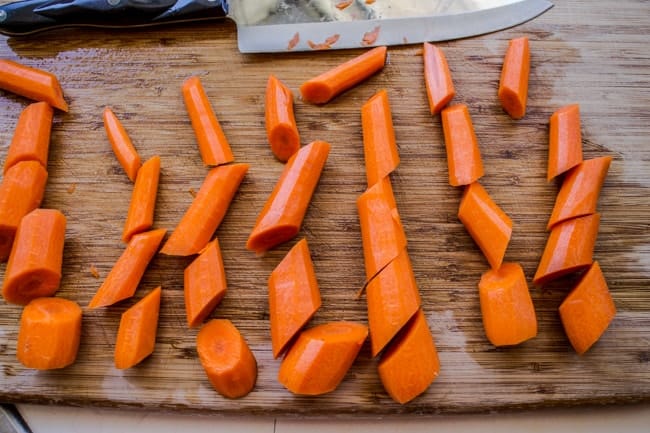 Peeled and chopped carrots on a brown cutting board. 
