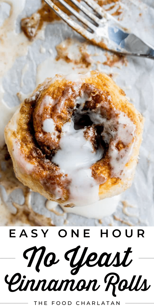 a flaky cinnamon roll with icing drizzled on top on parchment near a fork.