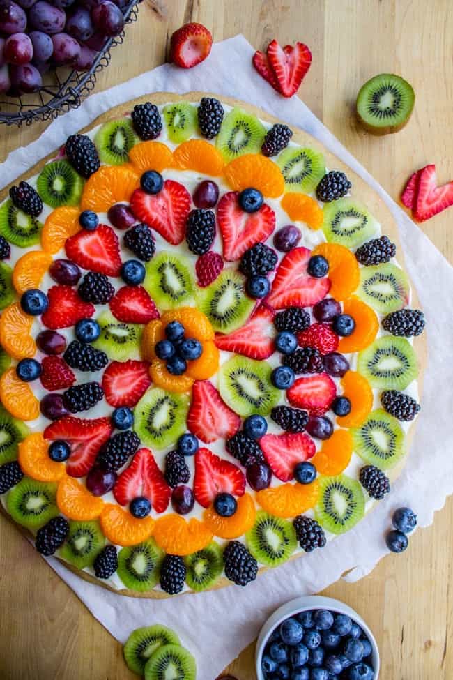 Overhead shot of sugar cookie based fruit pizza with strawberries, mandarin oranges, blueberries, kiwi, blackberries, and cream cheese frosting.
