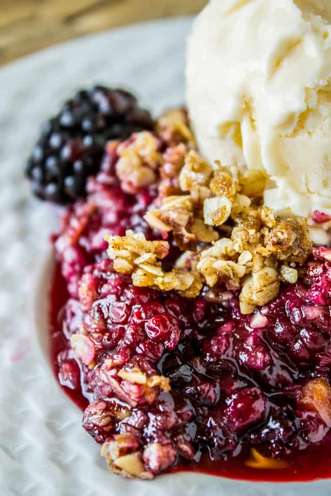 Blackberry cobbler on white dish with vanilla ice cream and fresh blackberry in background.