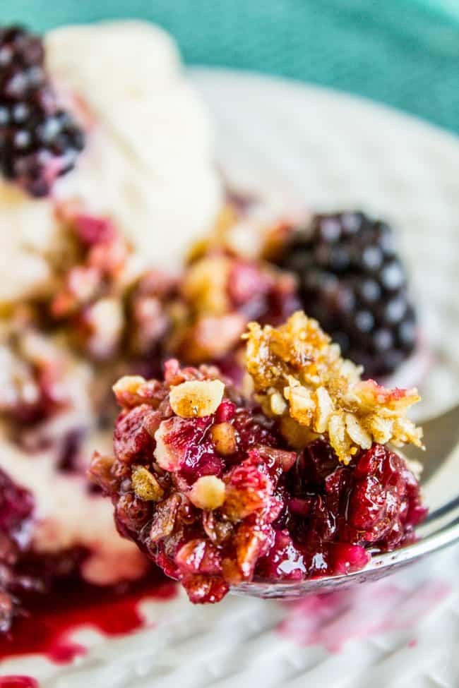 Bite of blackberry cobbler on spoon with plate in background.
