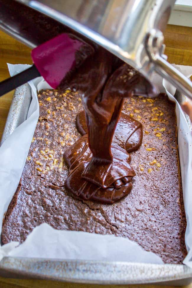 pouring warm fudge frosting on top of a pan of brownies.