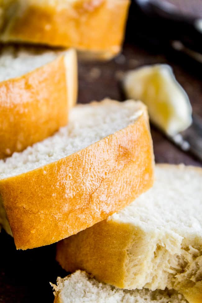 One Hour French Bread from The Food Charlatan. This delicious yeasty French bread recipe has only one 20-minute rise before going into a screaming hot oven for another 20 minutes. At the end you have golden crusty goodness just waiting to be slathered in butter or dipped in oil and balsamic! One hour, I promise!! #french #bread #homemade #easy #ideas #baguette #quick slices of homemade french bread with butter in the background.
