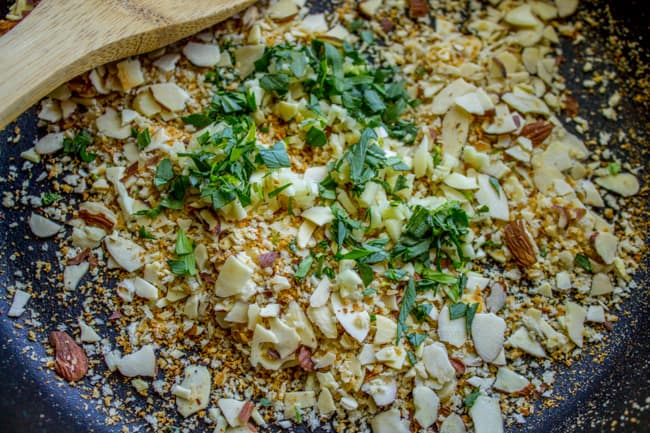 toasted breadcrumbs, garlic, and almonds in a pan with wooden spoon. 