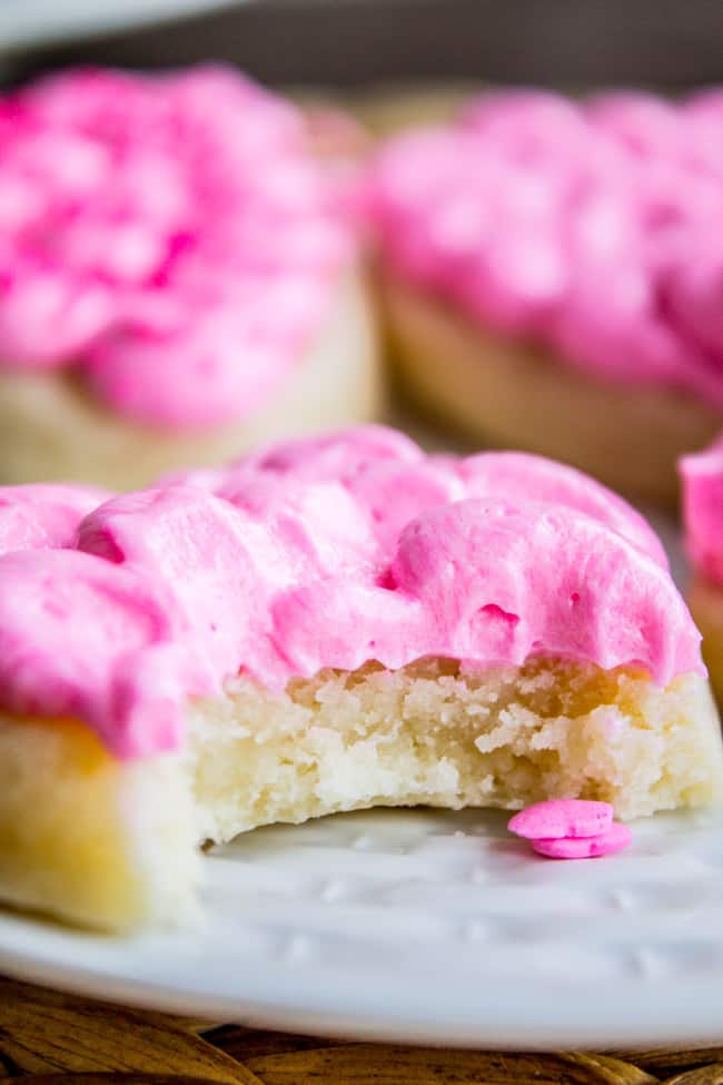 soft frosted sugar cookies with a portrait close-up of a bite taken out of cookies and pink buttercream frosting.