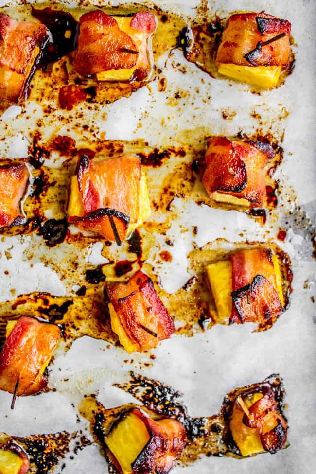 cooked bacon wrapped pineapple with a toothpick on parchment paper. 