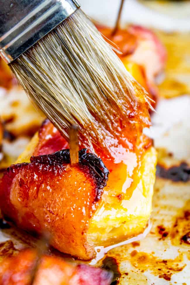 brushing glaze on bacon wrapped pineapple with a pastry brush. 