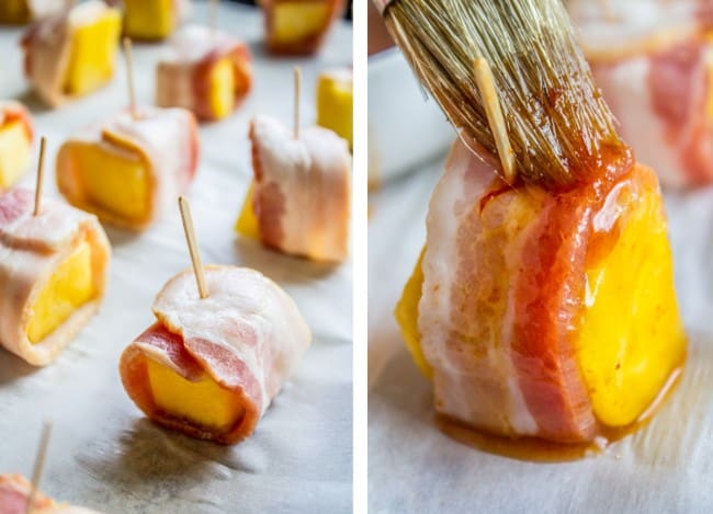 bacon wrapped pineapple, uncooked, and being brushed with glaze on a baking sheet. 