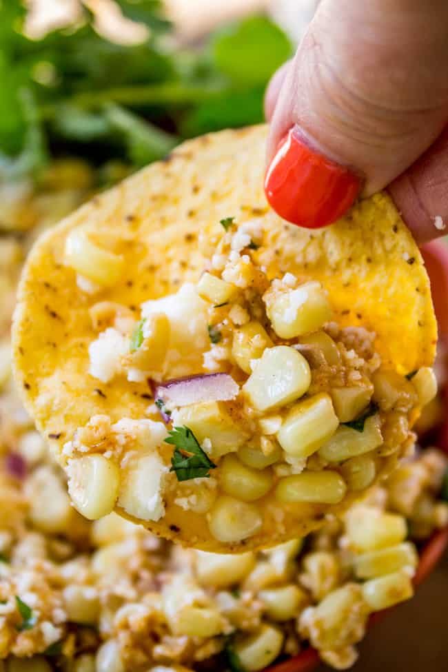 A woman´s hand dipping a tortilla chip into street corn dip.