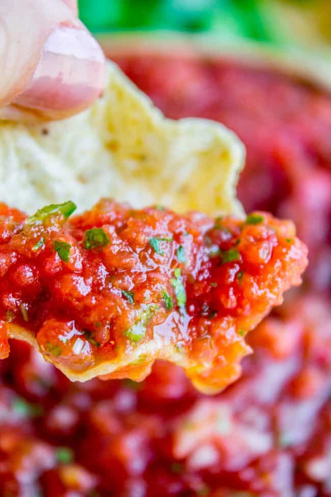 Close up of a hand dipping a tortilla chip into salsa. 