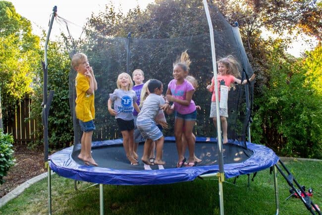 Kids jumping on a trampoline in a backyard. 