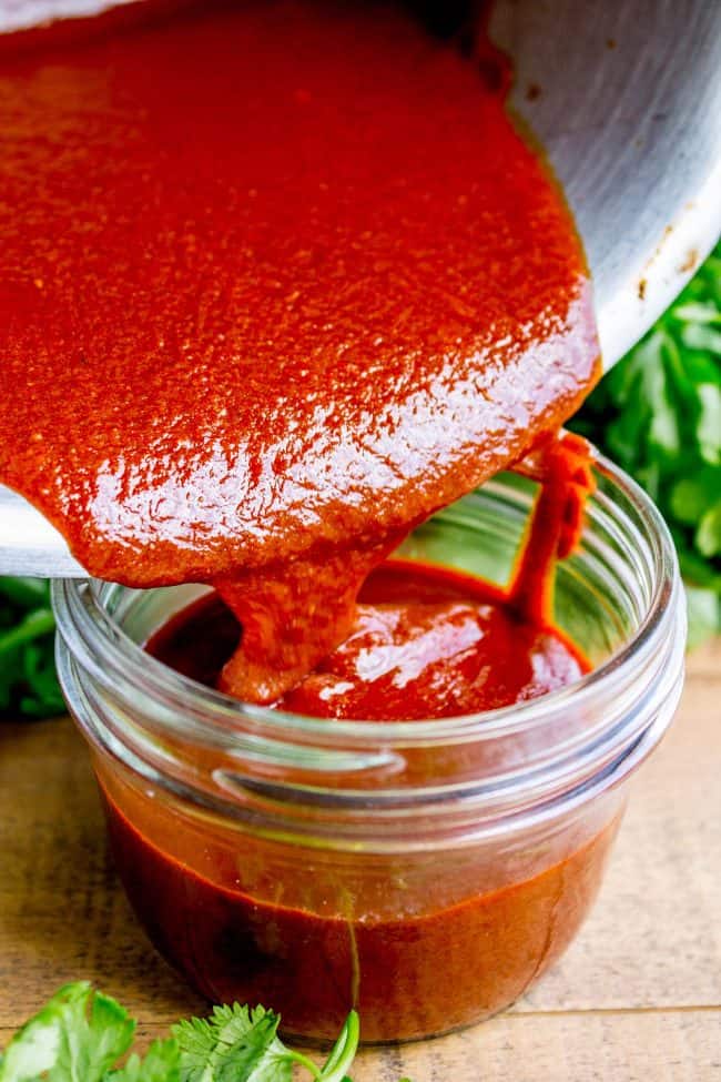 pouring homemade enchilada sauce into a mason jar.